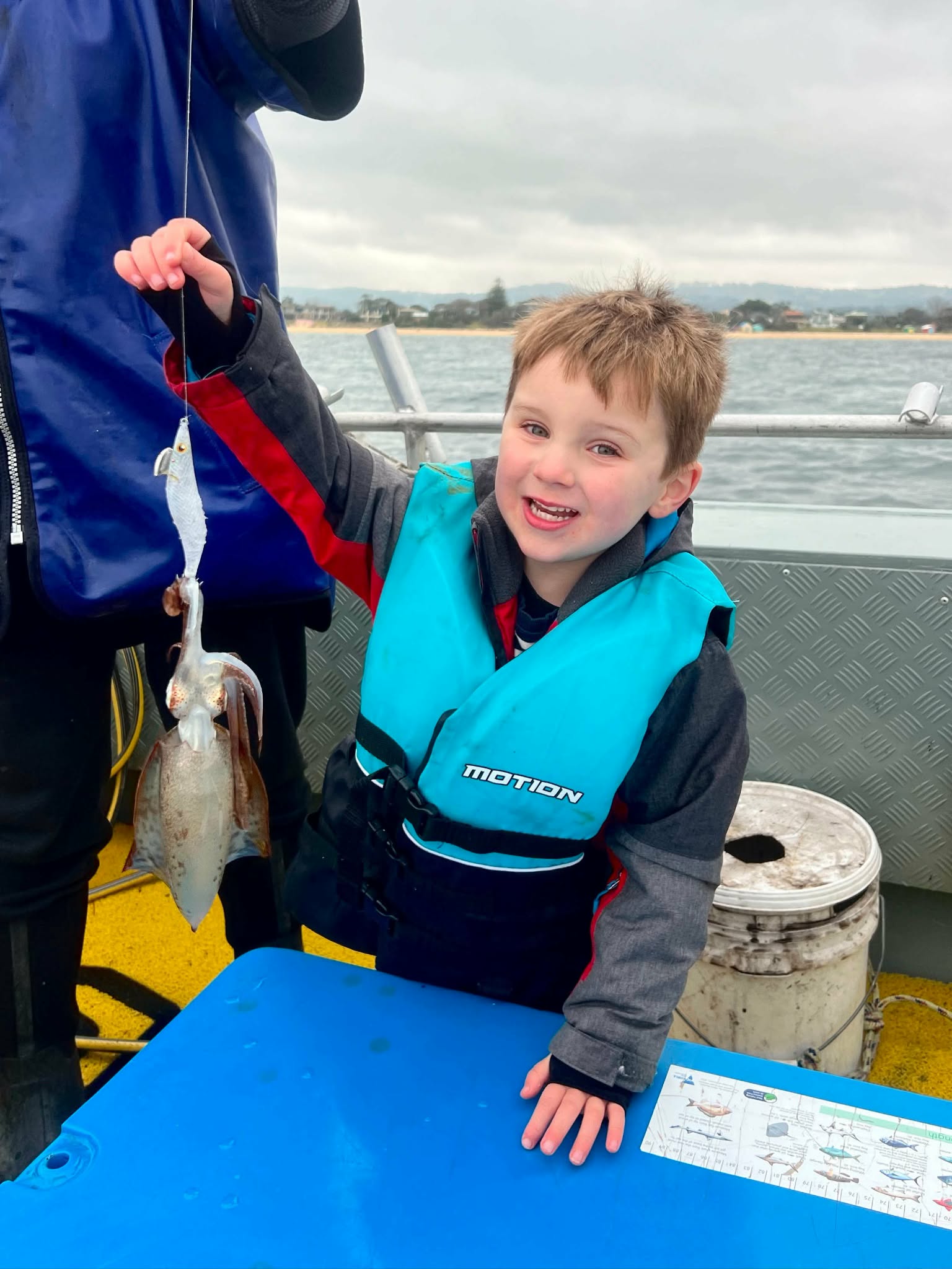 Young angler in a lifejacket proudly showing a squid