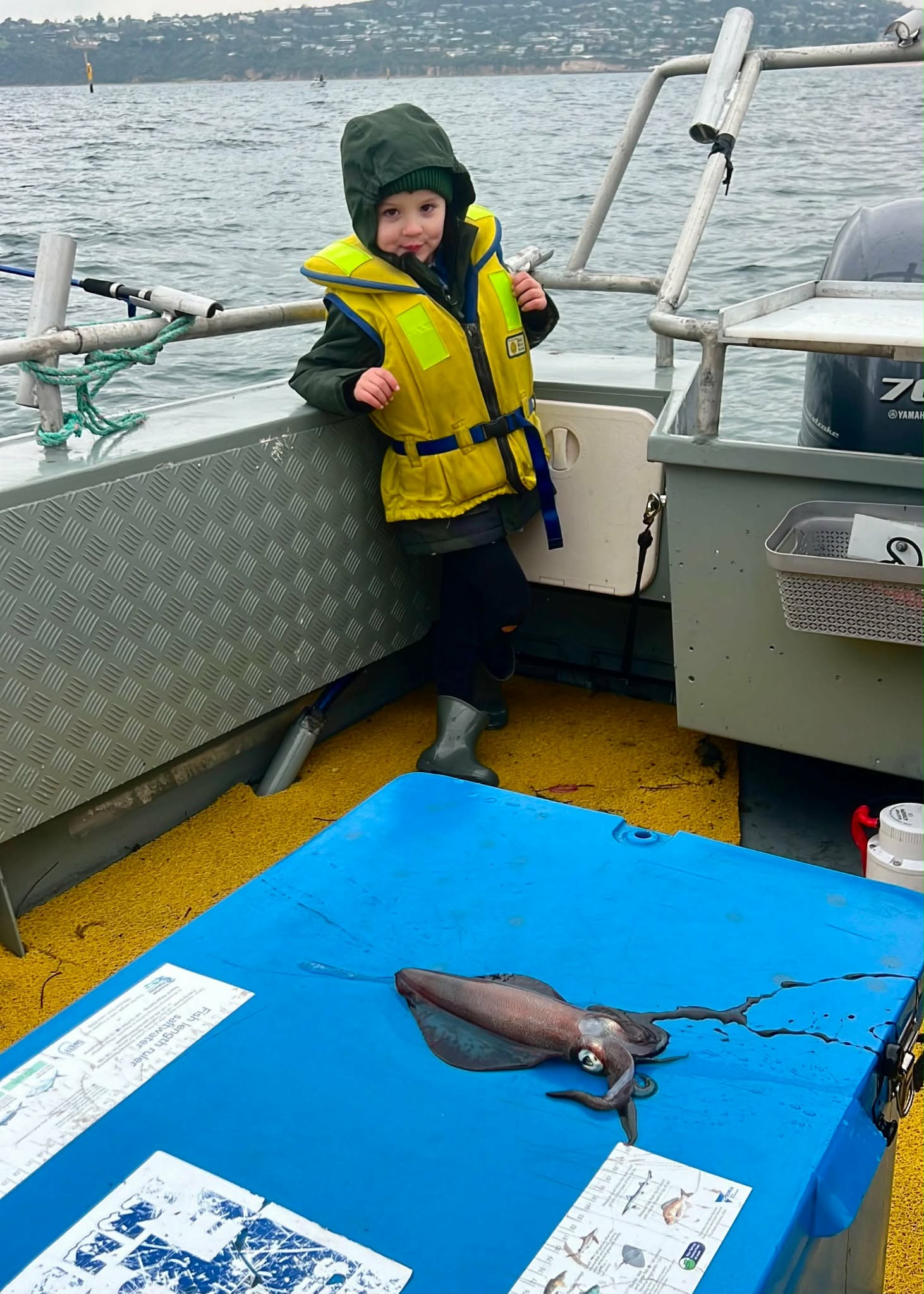 Young guest safely wearing a lifejacket beside a squid catch
