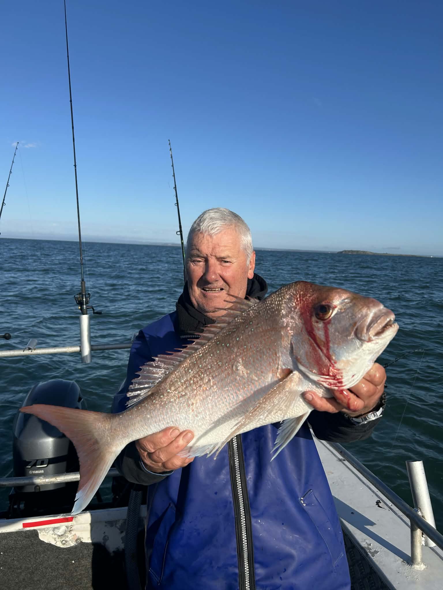 Angler holding a solid snapper with fishing rods behind